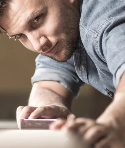 kanzlei-zeindl-partner-steuerberater-branchen-handwerk-verarbeitendes-gewerbe Ein Handwerker in Jeanshemd schleift konzentriert ein Werkstück. In der Brusttasche steckt ein Stift