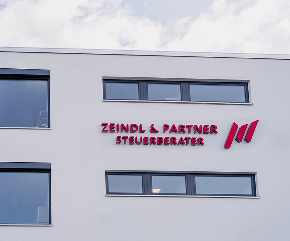 Außenansicht eines modernen Bürogebäudes mit dem roten Schriftzug ‚Zeindl & Partner Steuerberater‘ und einem stilisierten Logo an der Fassade