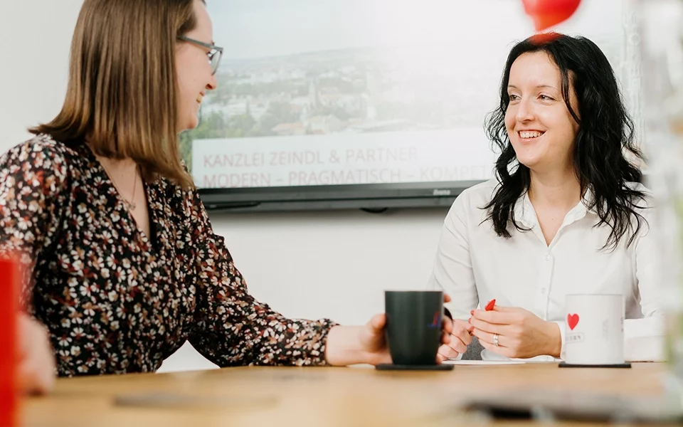 kanzlei-zeindl-partner-steuerberater-karriere-praktikanten-uebersicht Zwei Frauen sitzen an einem Tisch und unterhalten sich freundlich bei einer Tasse Kaffee