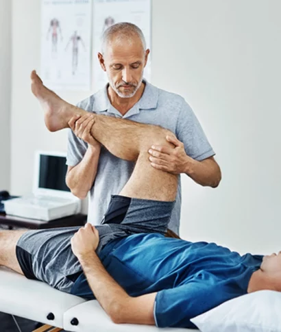 kanzlei-zeindl-partner-steuerberater-branchen-aerzte-heil-gesundheitsberufe Physiotherapeut behandelt einen Patienten auf einer Behandlungsliege, der Therapeut beugt vorsichtig das Bein des liegenden Patienten
