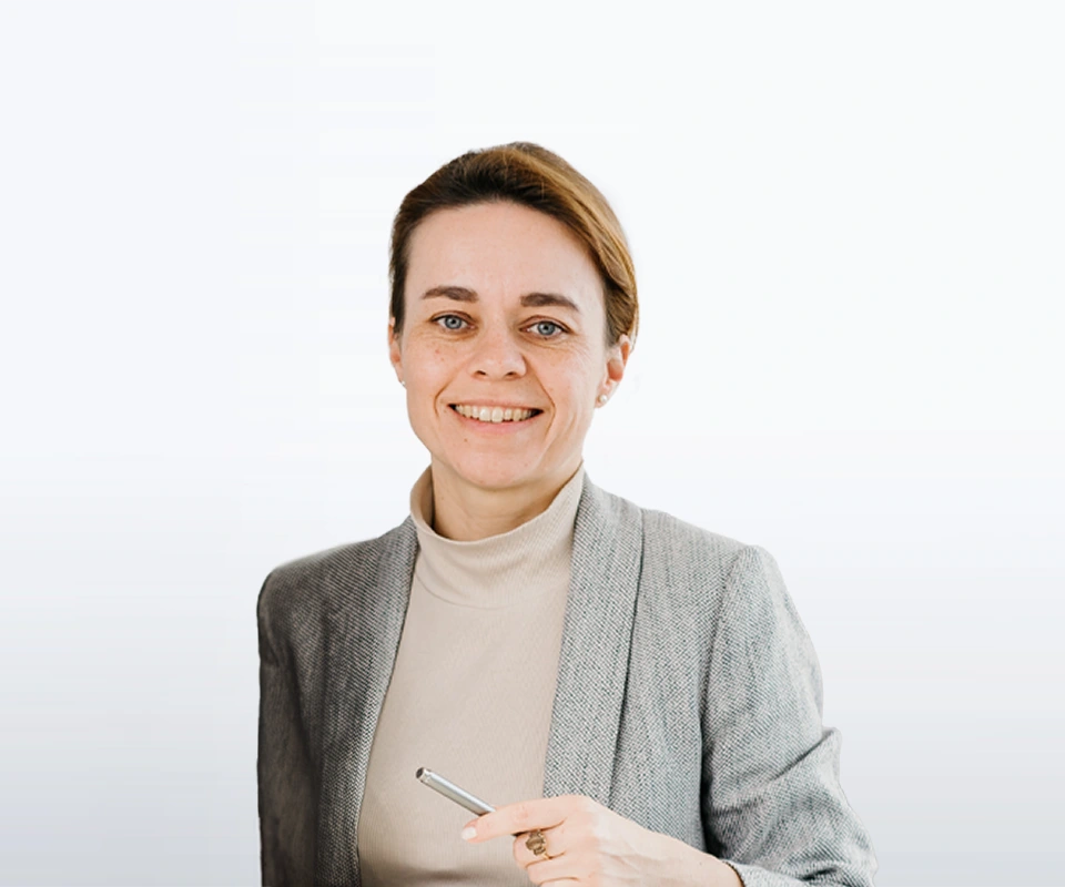 Portrait einer freundlich lächelnden Frau im hellem Rollkragenpullover und grauen Blazer hält einen Stift in der Hand