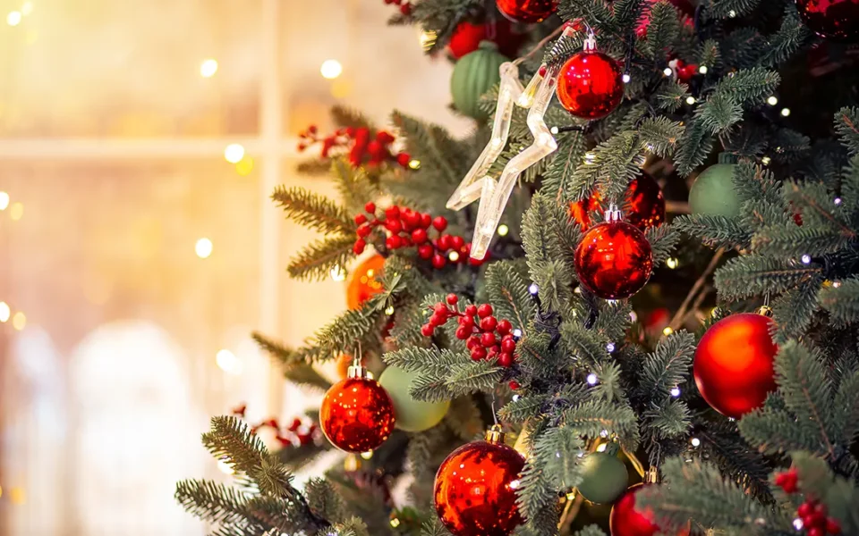Geschmückter Weihnachtsbaum mit roten und grünen Christbaumkugeln, Beerenzweigen und warmen Lichterketten in festlicher Innenraum-Atmosphäre
